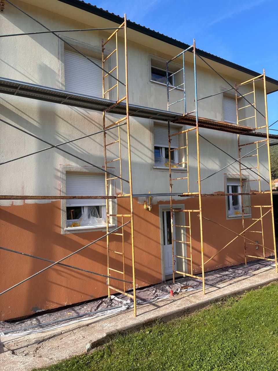 Fachada en obras, con andamio y pintura a falta del acabado